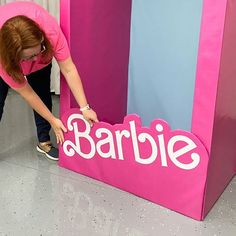 a woman in pink shirt leaning over a barbie sign