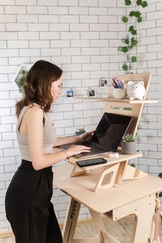 a woman standing in front of a wooden desk with a laptop on top of it