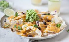 a white plate topped with nachos covered in cheese and black olives next to a glass of limeade