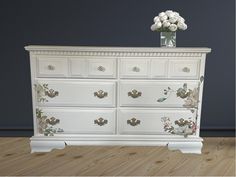 a white dresser with flowers painted on the top and bottom, sitting on a hard wood floor