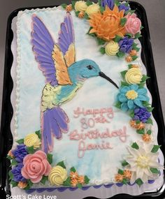 a birthday cake decorated with flowers and a humming bird