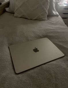 an apple laptop sitting on top of a bed in a room with white pillows and throw pillows