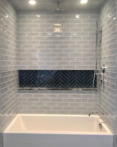 a bath tub sitting next to a window in a tiled bathroom with gray tile on the walls