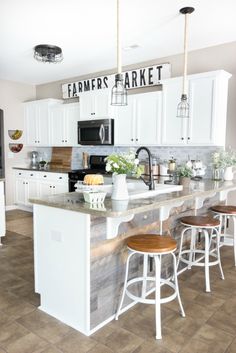 a kitchen with white cabinets and wooden stools in front of an island that has two bar stools on it