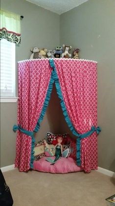 a child's bed with pink and blue curtains on the top, sitting in a room