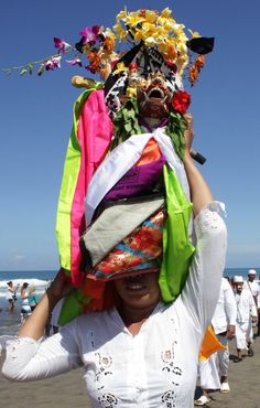 a woman is holding her head covered in colorful cloths and flowers on the beach