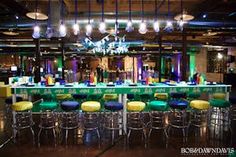 an indoor bar with green and yellow stools in the center, surrounded by lights