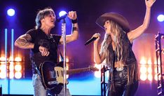 two people on stage with one holding a guitar and the other singing