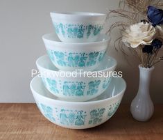 a stack of bowls sitting on top of a wooden table next to a vase with flowers