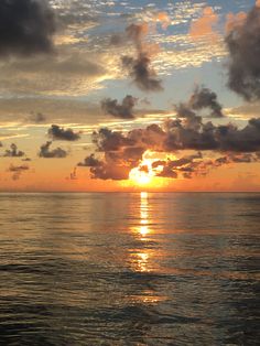 the sun is setting over the ocean with clouds in the sky and on the water