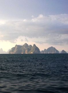 an island in the middle of the ocean with mountains in the backgrouds