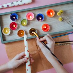 two hands are holding candles and painting them