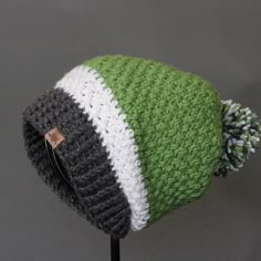 a green and white knitted hat sitting on top of a wooden stand next to a gray wall