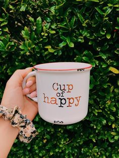 a hand holding a cup with the words cup of happy on it in front of some bushes