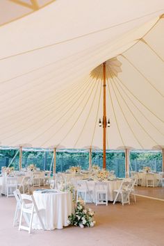 the inside of a tent with tables and chairs set up for a wedding reception under an umbrella