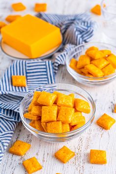 two glass bowls filled with yellow cubes on top of a white wooden table next to a blue and white towel