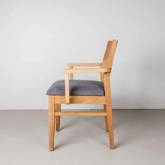 a wooden chair with grey upholstered seat and backrest, against a white wall