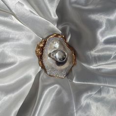 two wedding rings sitting on top of an oyster shell in white satin with gold accents