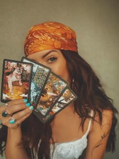 a woman holding up four cards in front of her face and wearing a bandana