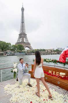 a man kneeling down next to a woman in front of the eiffel tower