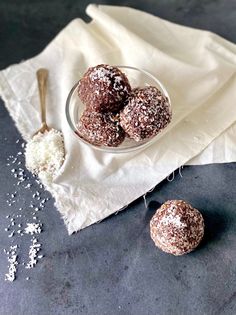 three chocolate donuts are in a glass bowl on a white napkin next to two spoons