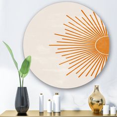 an orange and white sunburst is on the wall above a table with vases