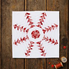 a white piece of paper with red designs on it next to some spools of thread