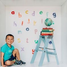 a young boy sitting on the floor in front of a wall with letters and a ladder