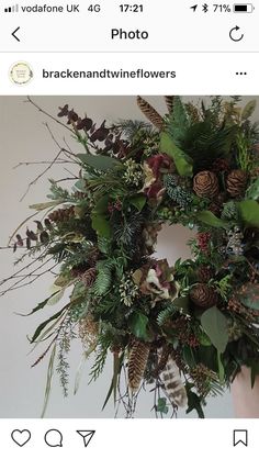 a wreath with pine cones and greenery hanging from the front of a white wall