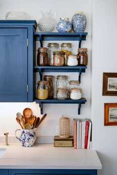 a kitchen with blue cabinets and shelves filled with jars, utensils and other items