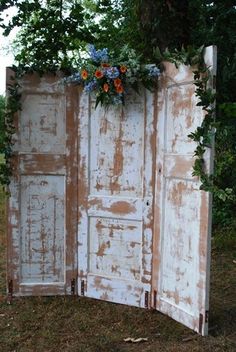 an old door with flowers growing out of it in the middle of a grassy area