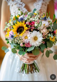 a bride holding a bouquet of sunflowers and greenery