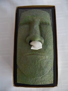 a green face in a cardboard box with a white piece of paper sticking out of it's mouth