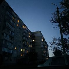 an apartment building lit up at night with the lights on and cars parked in front