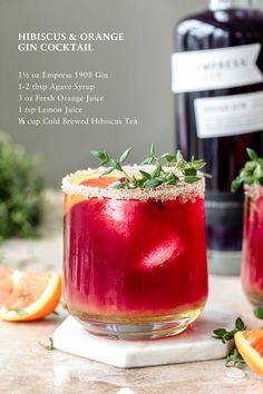 two glasses filled with red liquid and garnished with herbs next to a bottle of gin cocktail