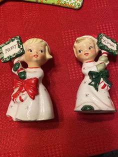 two ceramic figurines sitting on top of a red cloth covered table next to each other