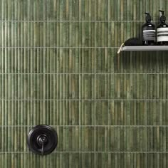 a bathroom with green tile and black shower faucet next to shelf on the wall