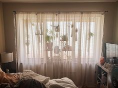 a bedroom with a bed, dresser and window covered in sheer curtained drapes