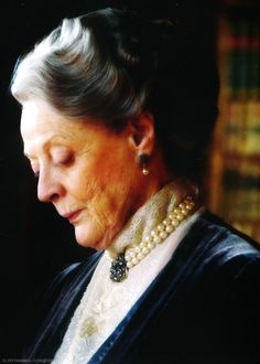 an older woman wearing pearls looking down at her cell phone