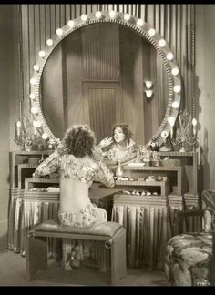 a woman sitting at a dressing table in front of a mirror with lights on it