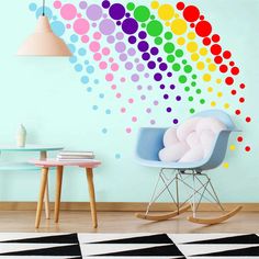 a room with a rocking chair, table and rainbow wall decal