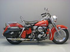 a red and black motorcycle is parked on the floor next to a gray wall in an empty room