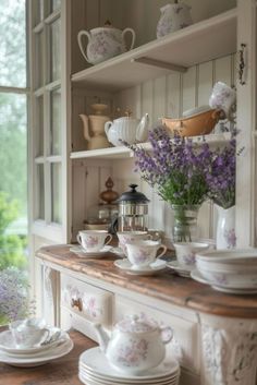 an old fashioned china cabinet with purple flowers in the vases and dishes on it