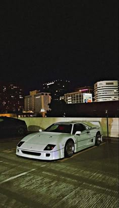 a white car parked on top of a parking lot next to tall buildings at night