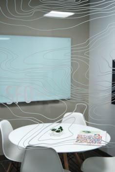 a white table and chairs in front of a glass wall with an abstract design on it