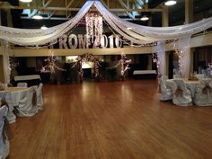 an empty ballroom with tables and chairs covered in white linens, decorated with fairy lights