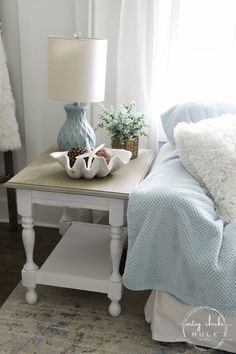 a bedroom with a bed, nightstand and lamp on it's side table in front of the window