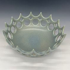 a green bowl with holes in it on a white tableclothed surface and gray background