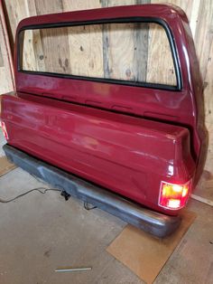 the back end of a red car in a garage with wood planks behind it