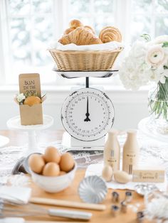 a table topped with bread and pastries on top of a kitchen scale next to a bowl of eggs